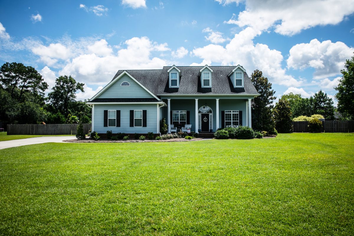 pale blue house with siding on a large lot with traditional windows and shutters in a subdivision in the suburbs on a bright sunny blue sky day