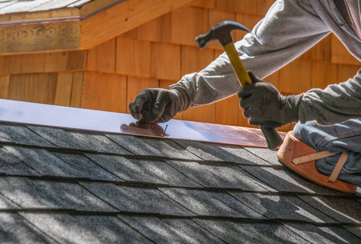 Man installing asphalt roof with nail gun