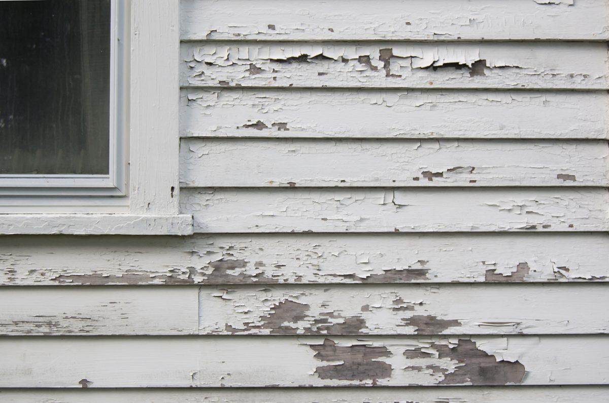 Peeling white paint on a calpboard hose with part of window