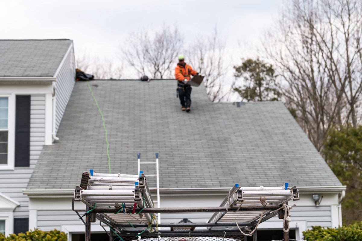 House during day over garage with truck, gray color Single Family Home and man walking on roof shingles and ladder during repair