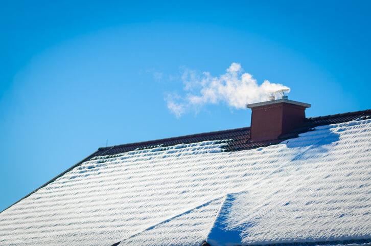 White smoke comes out of a house's chimney on a winter day.