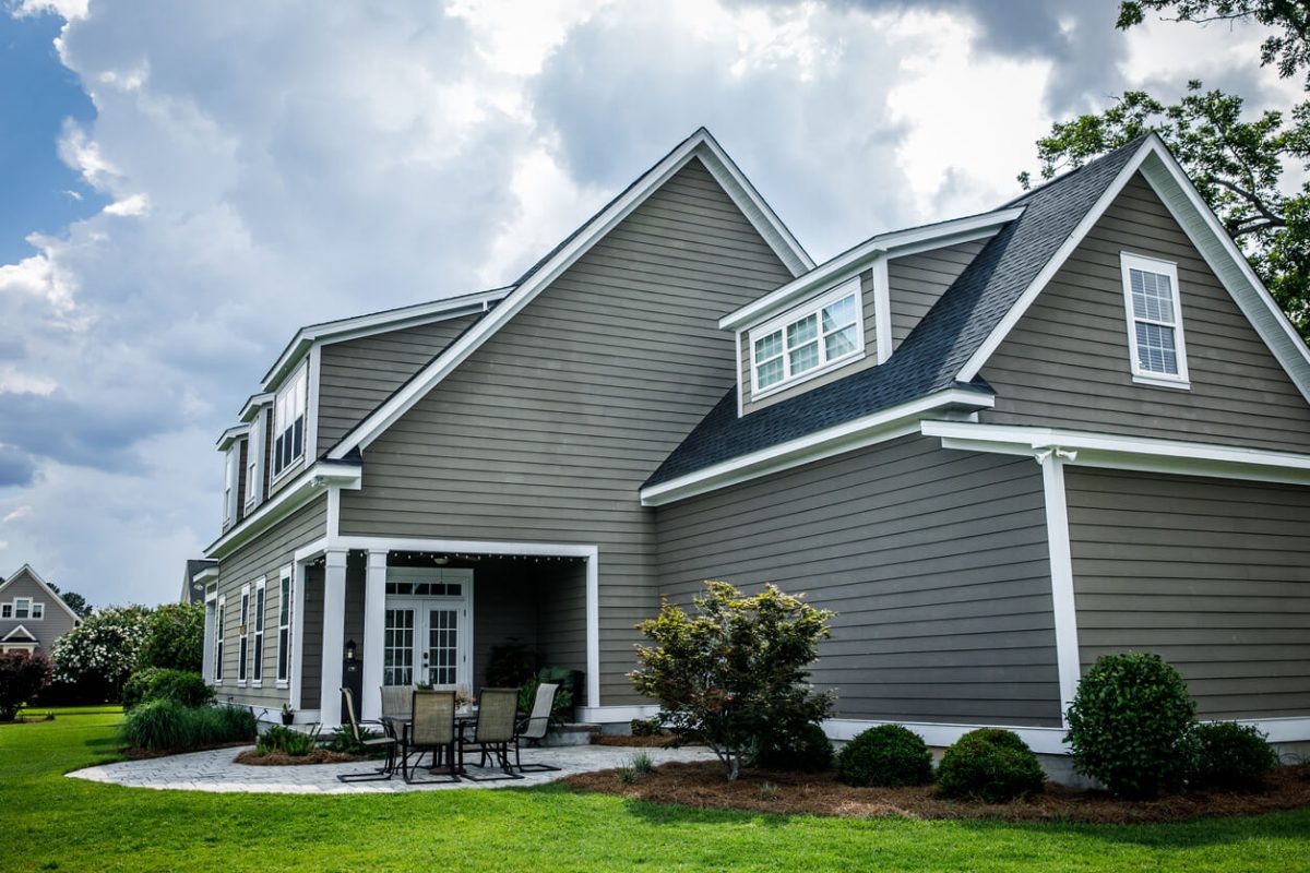 Side and rear view of tan craftsman home house with siding and a porch and patio area. This is a new construction home with an open floor plan