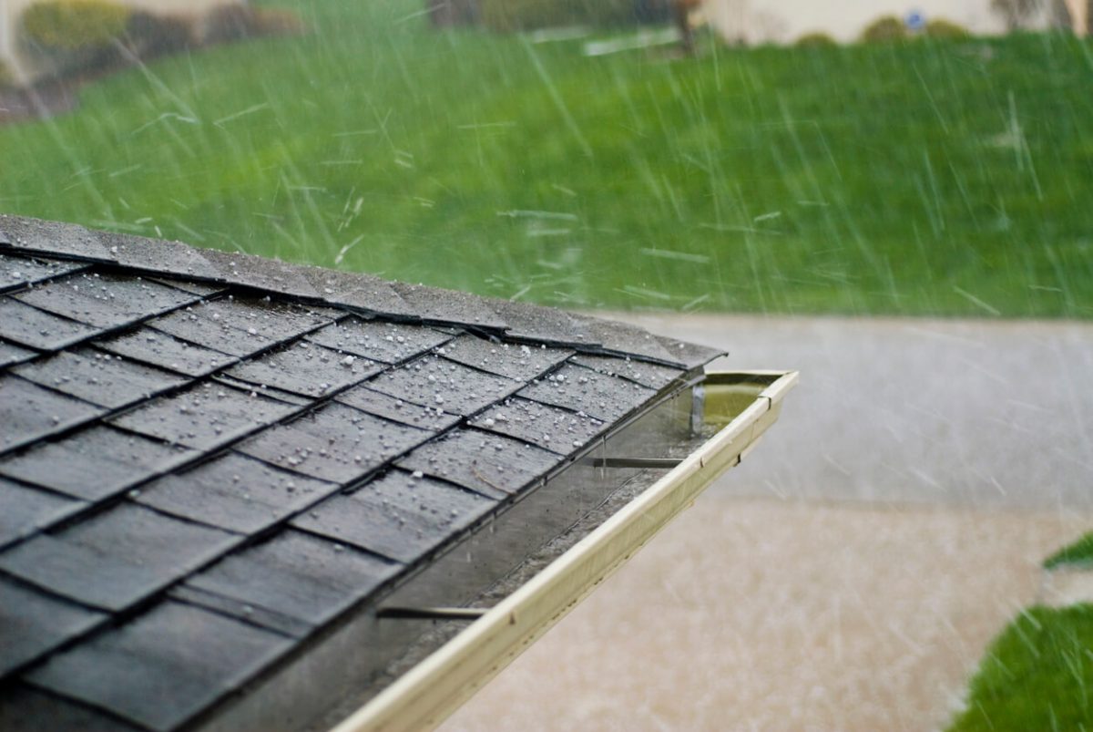 Hail Stones Hitting a Roof During a Storm shows pea-sized ice chunks bouncing off a portion of a house roof.