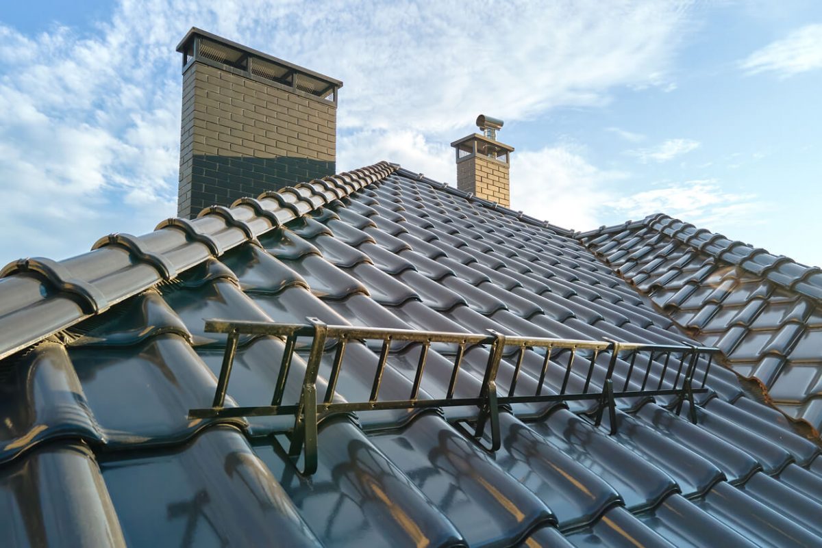 Closeup snow guard for safety in winter on house roof top covered with ceramic shingles. Tiled covering of building.