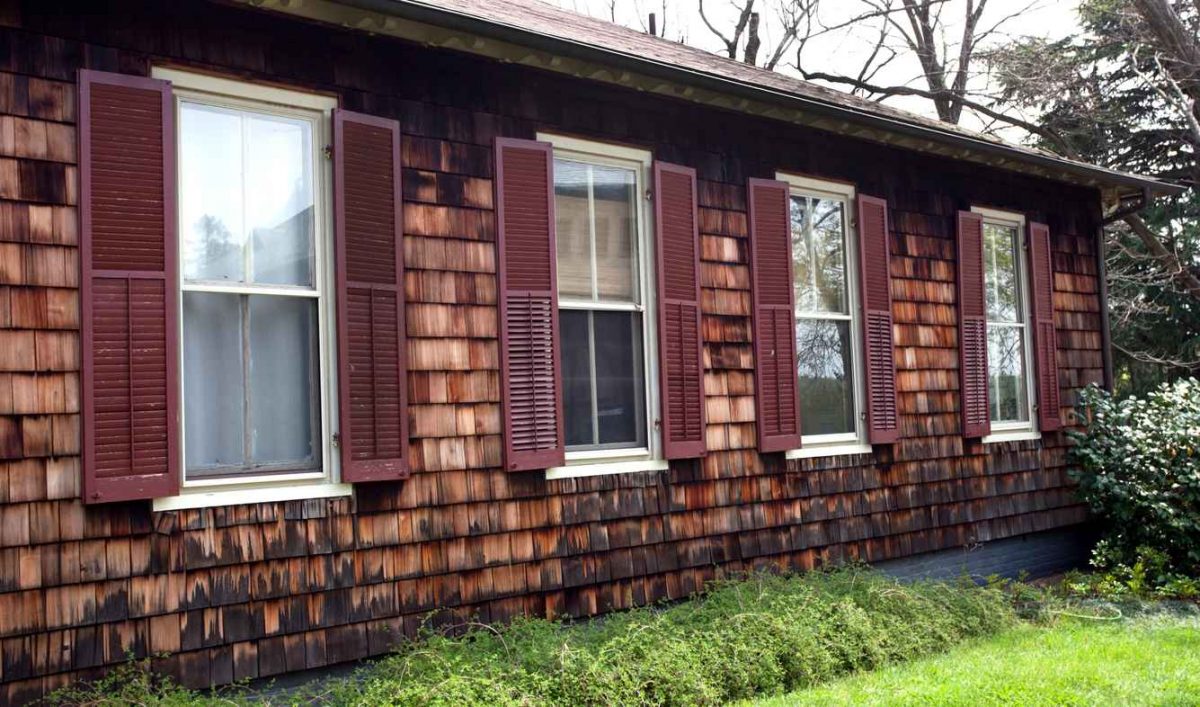 Side of home with cedar siding and brown shuttered windows.
