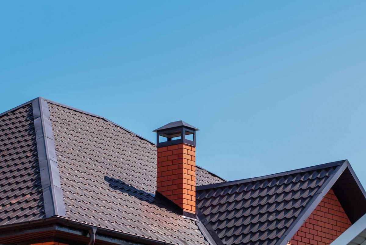 The exterior of the roof of a country house against the sky. Brick chimney pipe on metal roof of a private house. Individual heating system. Rain gutter.