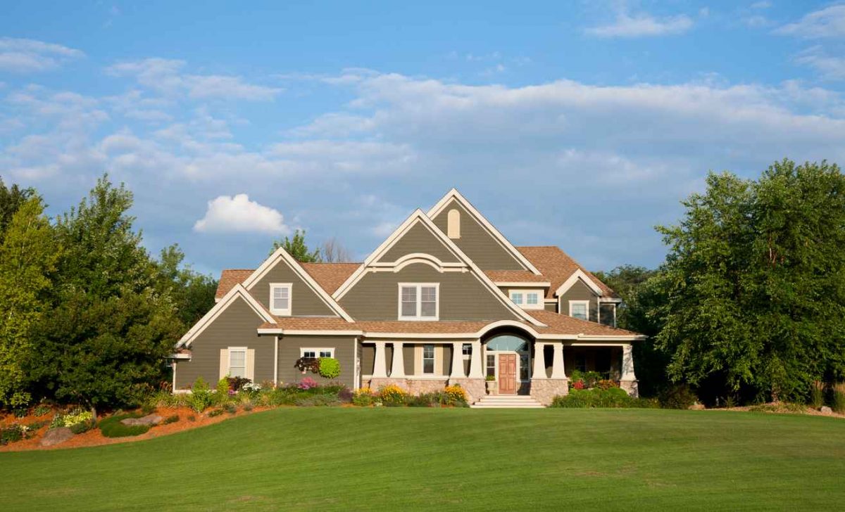 Country Estate/Cottage: Pillars with stone, cedar shakes, hardie board siding and cedar roof with beautiful landscaping against an evening clearing blue sky.